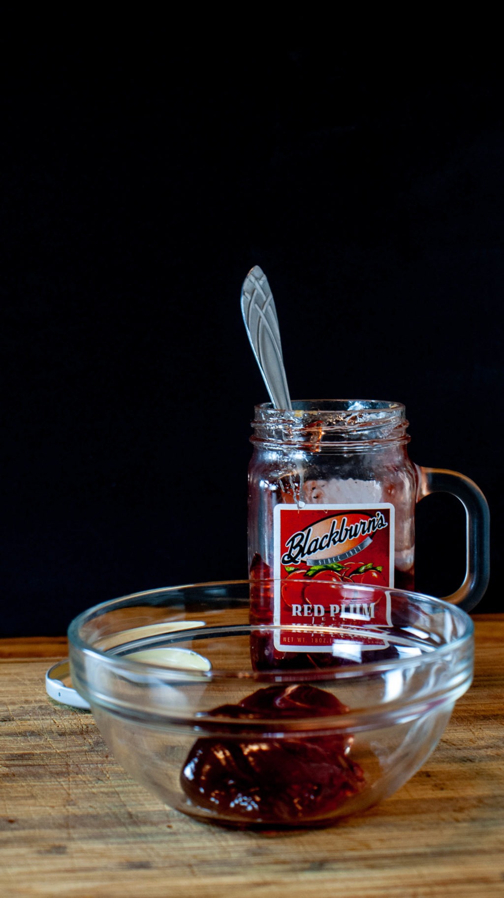 Plum jelly in a glass bowl with jelly jar in the background