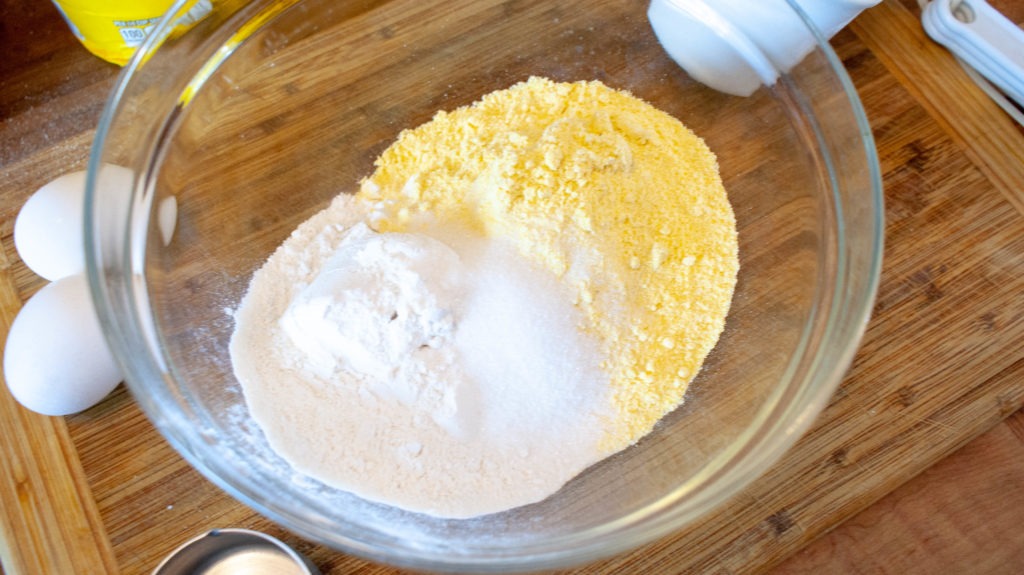 Flour, cornmeal, sugar, and salt in a bowl surrounded by ingredients for hoecakes