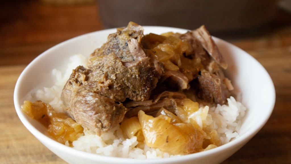 Beer and onion braised pork roast over white rice in a bowl