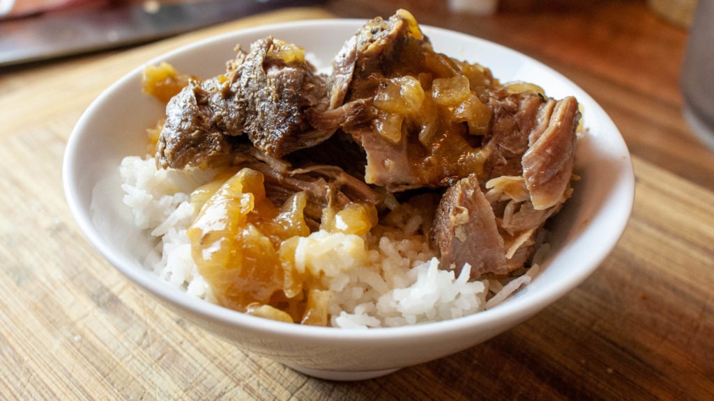 Beer and onion braised pork roast over white rice in a bowl