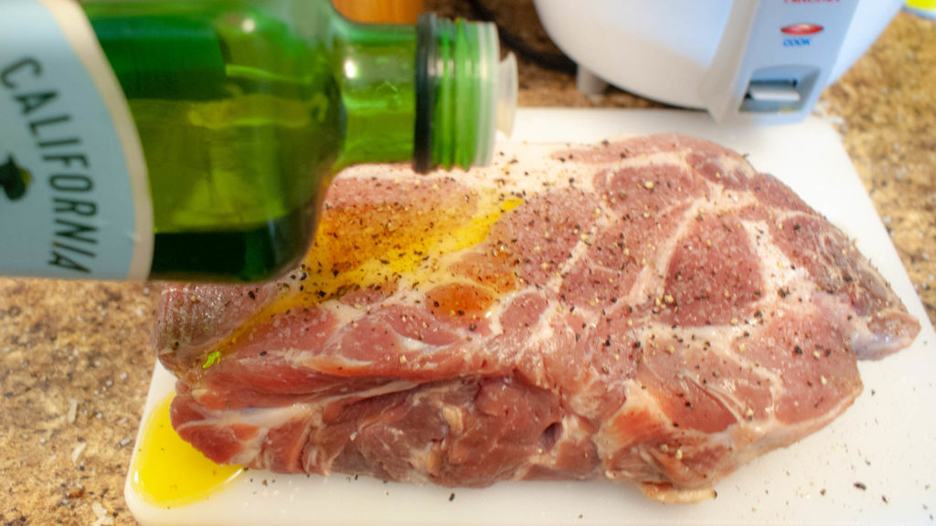 seasoned pork roast being covered in olive oil
