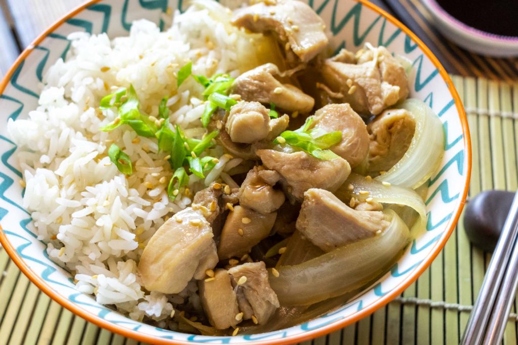 Simmered chicken and onions on top of rice with green onions